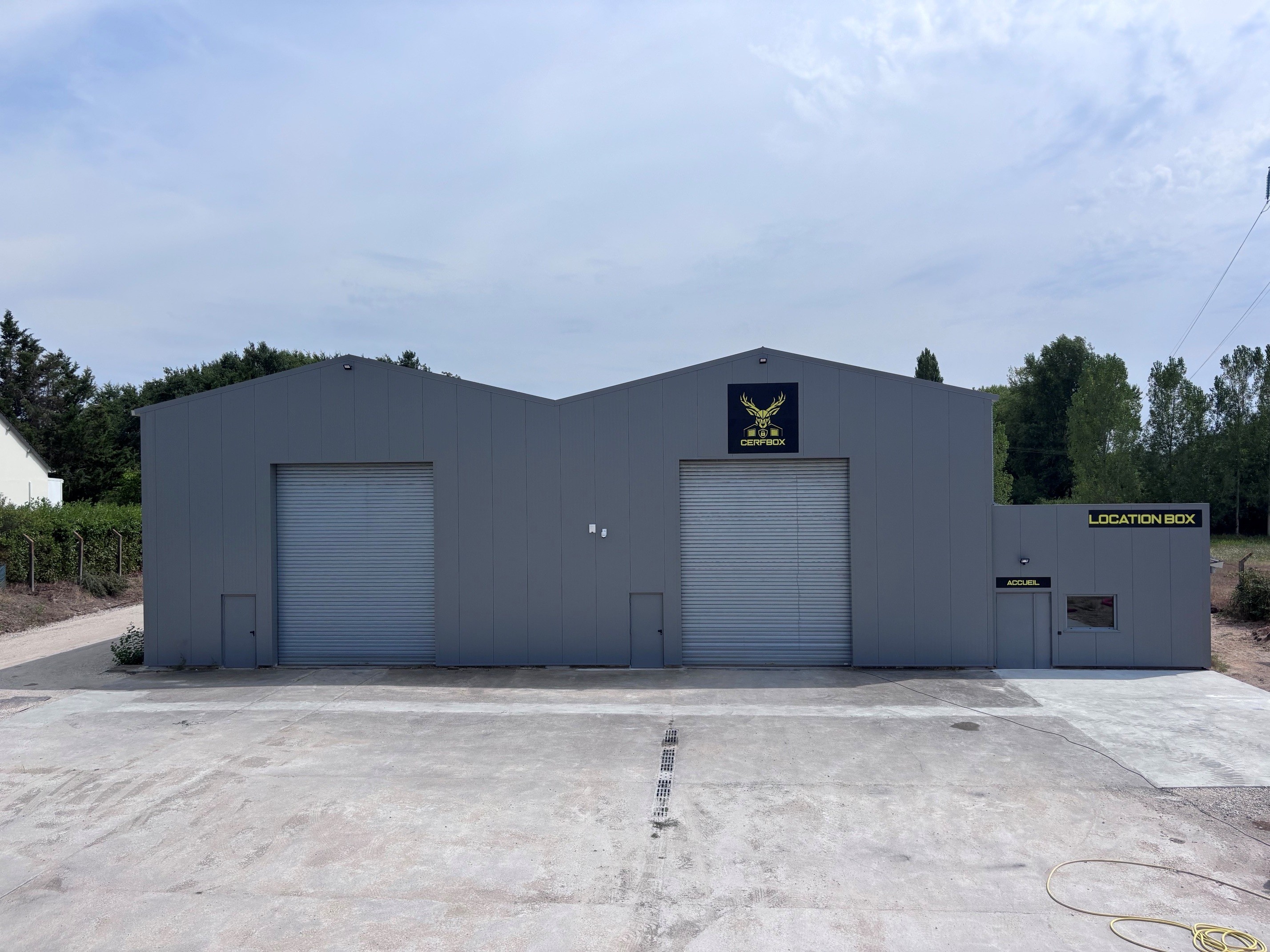 Façade grise du centre de location de box de stockage Cerfbox avec portes sectionnelles et zone d'accueil.